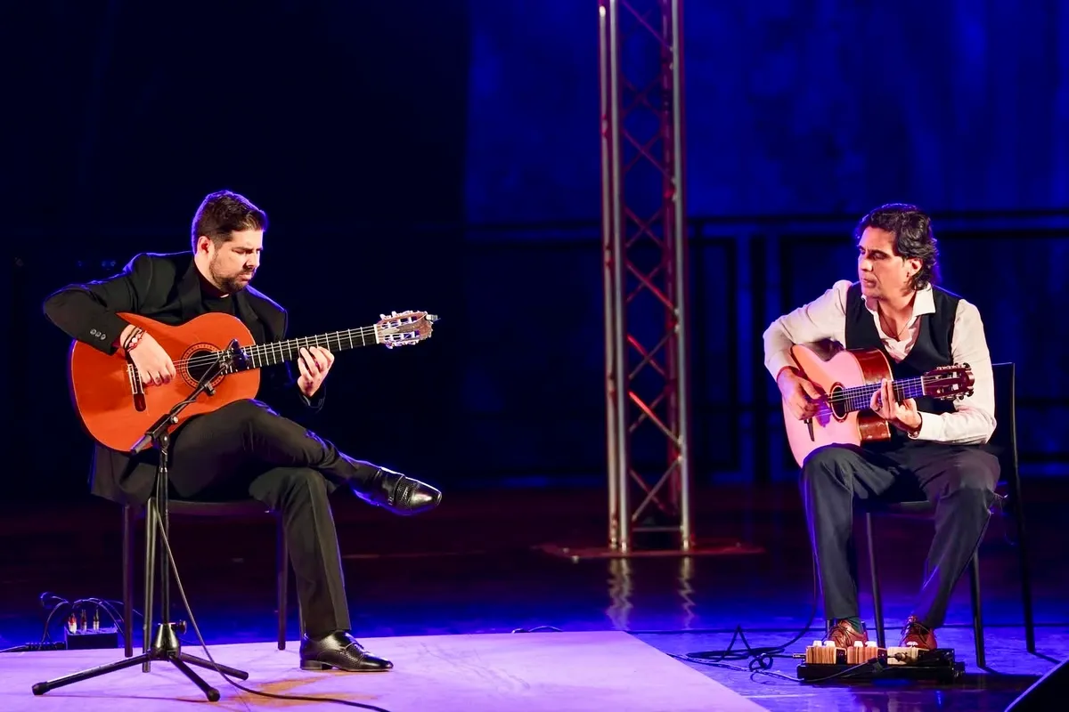 Two guitarists performing a duet on a blue-lit stage