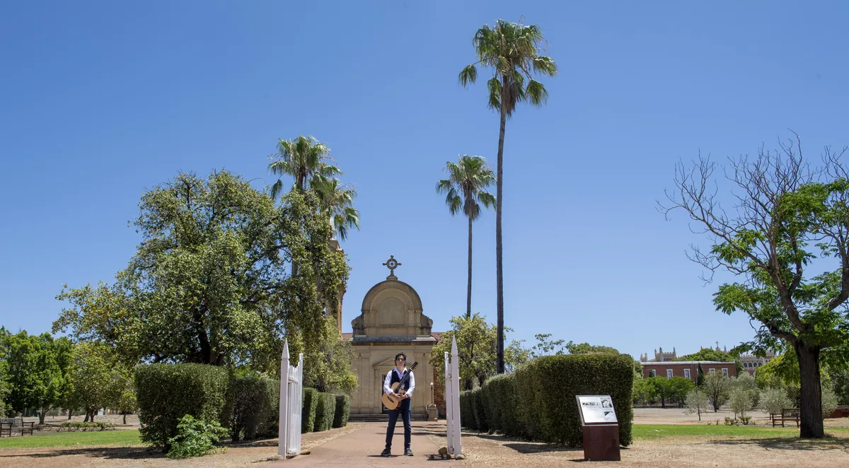 Ernesto Castillo with guitar on a path lined with palms