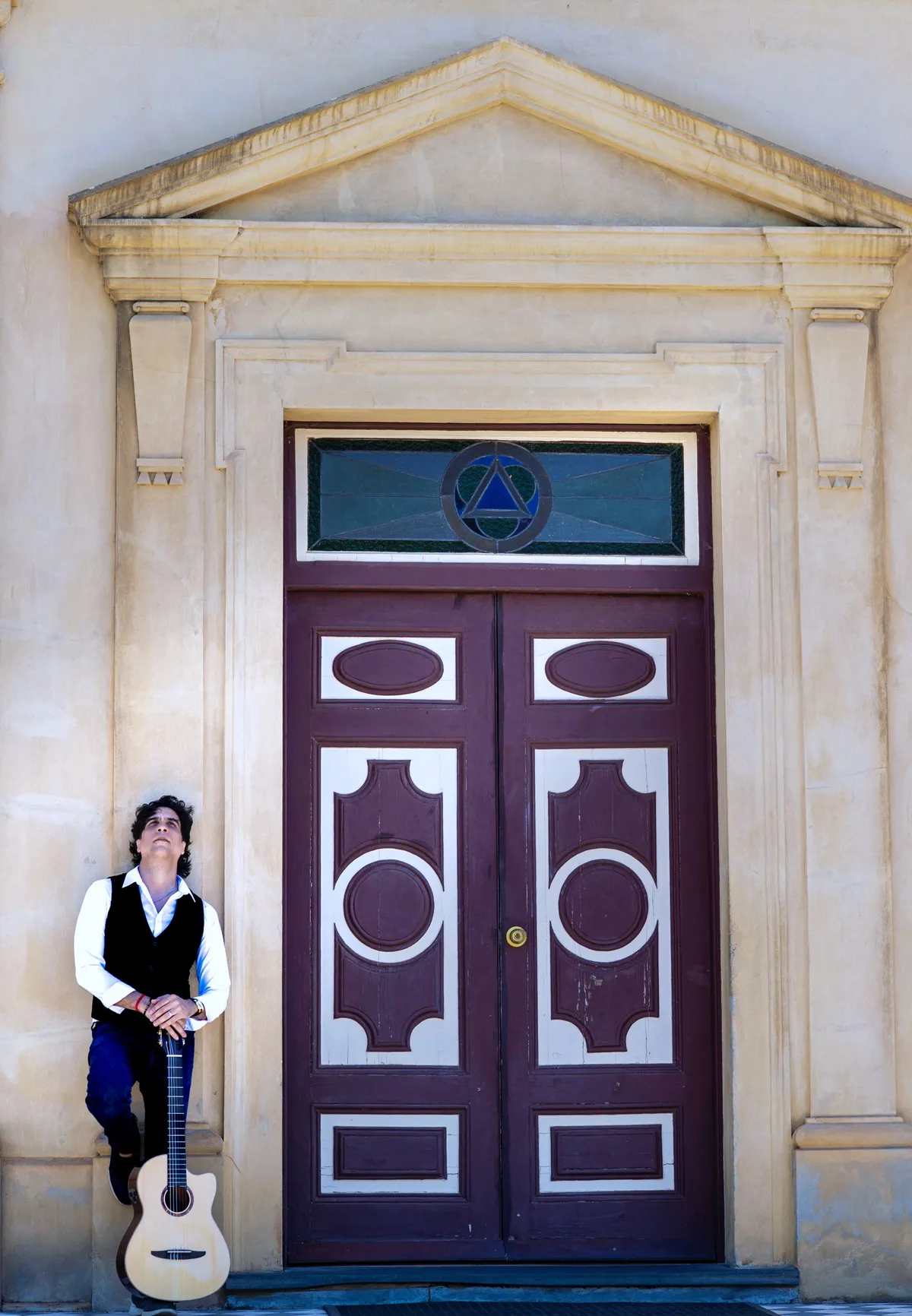 Ernesto Castillo leaning beside a tall purple heritage door with his guitar