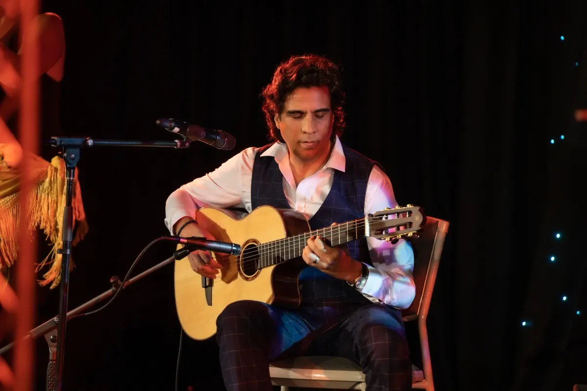 Ernesto Castillo playing guitar beside a flamenco shawl on stage