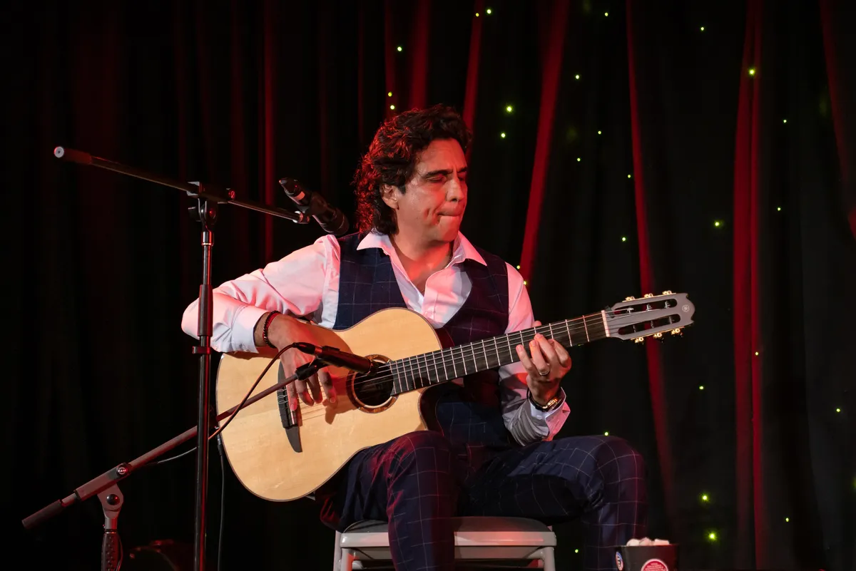 Ernesto Castillo playing nylon-string guitar in front of a red curtain